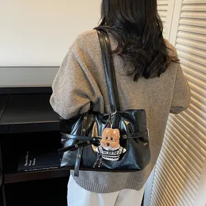 Détail d'un sac cabas noir brillant avec œillets métalliques et pendentif chien en peluche
