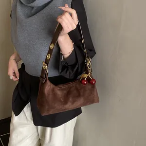 Sac vintage marron mat avec bandoulière à œillets métalliques et breloque cerise sur modèle