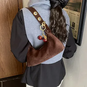 Détail du sac demi-lune en daim marron avec bandoulière à œillets et pendentif cerise