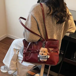 Détail du sac à bandoulière rouge brillant avec boucles et pendentif ours en peluche