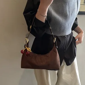 Détail du sac hobo en daim marron foncé avec anneaux dorés et breloque cerise décorative