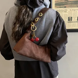 Détail d'un sac cabas en daim marron avec œillets métalliques et charm cerise