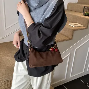 Détail du sac demi-lune en daim marron foncé avec un pendentif décoratif en cerise rouge