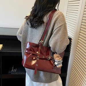 Détail d'un sac cabas bordeaux brillant avec pendentif ours et bandoulière réglable