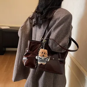 Gros plan d'un sac cabas en cuir verni marron brillant avec un charme d'ours en peluche