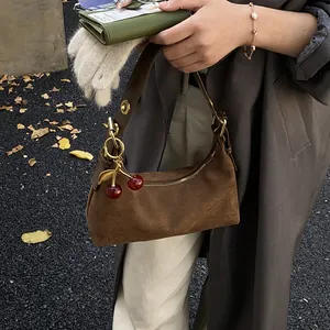 Gros plan du sac hobo en daim marron vintage avec un charmant pendentif cerise rouge