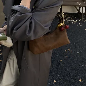 Détail du sac sous l'aisselle en daim marron foncé avec charme cerise métallique