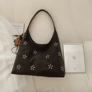 Détail d'un sac cabas vintage marron brodé de fleurs avec un pendentif en bois à côté d'un iPad