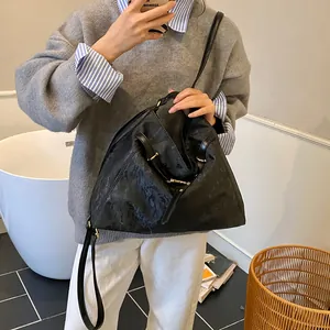 Detail of a large black leather hobo bag with gold hardware worn by a model in a room