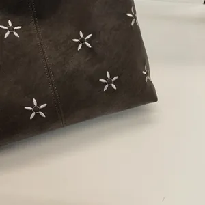 Gros plan d'une broderie florale blanche sur un cabas en cuir marron foncé aux coutures fines