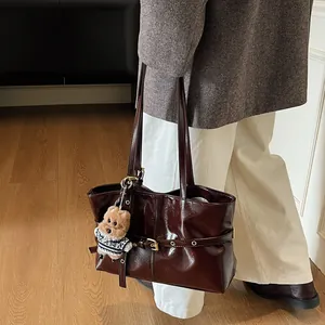 Détail du sac cabas en cuir verni marron foncé avec boucle dorée et breloque ours en peluche