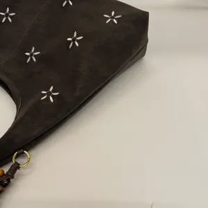 Détail du cabas en daim marron avec broderie florale et pompon en perles sur anneau doré