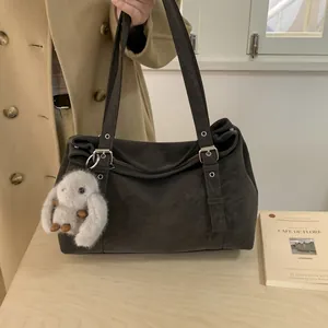 Vue détaillée du sac Boston en daim marron foncé avec boucles métalliques et breloque lapin
