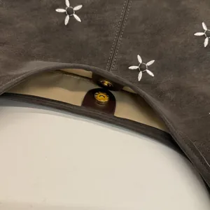 Détail du sac cabas en daim marron avec broderie florale et fermeture aimantée dorée