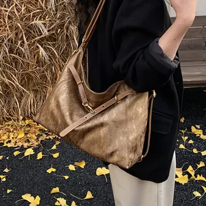 Close-up of vintage bronze tote bag with brown leather straps on fallen autumn leaves