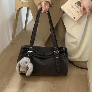 Détail macro du sac à bandoulière en daim marron foncé avec boucles et breloque lapin en peluche