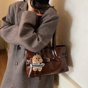 Détail du sac cabas marron brillant avec charm ours sur un manteau anthracite