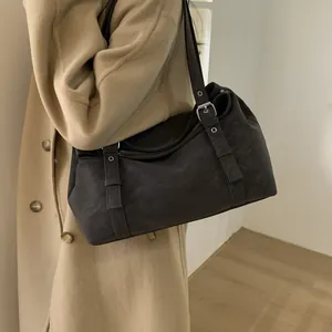Détail d'un sac polochon en daim marron foncé avec deux sangles sur l'épaule du mannequin