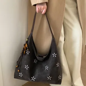 Détail du sac cabas vintage avec broderies florales, texture en daim et pompon en perles bois