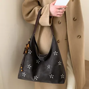 Détail d'un sac cabas marron en cuir avec broderie florale et pompon sur modèle