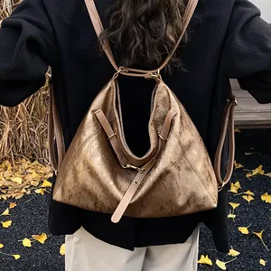 Detail of metallic bronze hobo backpack with thin brown straps on autumn leaves background