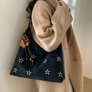 Détail de broderie florale et breloque en bois sur un sac cabas noir vintage