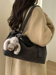 Sac hobo en daim marron foncé avec breloque lapin porté par un mannequin en manteau de laine