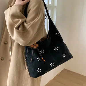 Détail du sac bandoulière en daim noir avec broderie florale et pendentif à fleurs