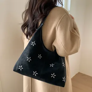 Vue détaillée du sac croissant noir avec broderie florale porté sur un manteau en laine