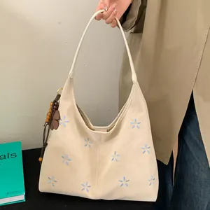 Détail du sac cabas en cuir crème avec broderie florale bleue et breloque en bois