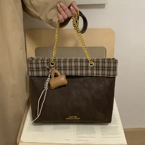Detail der Vintage-Plaid-Tragetasche mit Goldkette und Mini-Taschenanhänger auf einem Holzstuhl
