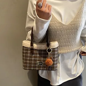 Detalle del bolso tipo cubo de cuadros con ribete de lana de oveja y placa de logo metálica