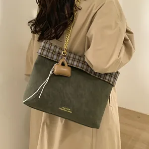 Grüne Wildleder-Tragetasche mit Karomuster und Goldkette, am Modell für das Styling gezeigt
