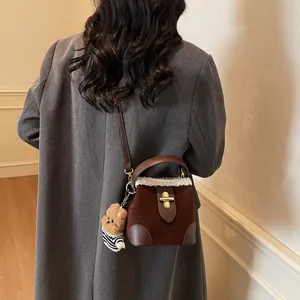 Détail du sac seau en daim marron avec bordure en fourrure et peluche sur manteau en laine