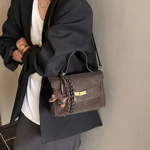 Detalle de bolso vintage marrón oscuro con dije de teckel sobre blazer negro