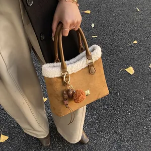 Detalle de bolso de ante marrón con ribete de felpa blanca y un colgante de peluche