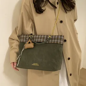 Detail der grünen Wildledertasche mit Karomuster und Goldkette, getragen zum beigen Trenchcoat