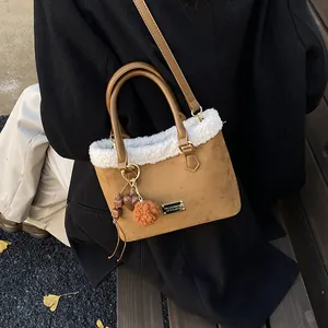 Detalle de borde de pelo sintético y logo dorado en bolso de ante marrón con adornos