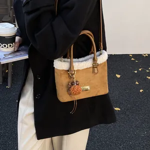 Detalle de bolso tipo cubo de felpa con ante marrón, ribete de borreguillo y pompón