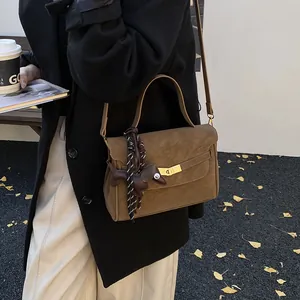 Detalle del bolso de ante marrón con cierre dorado y colgante de caballo en parque otoñal