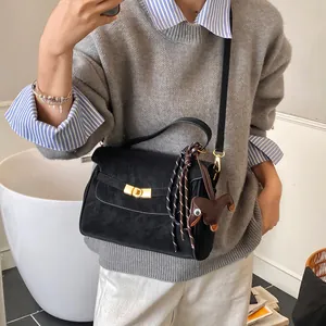 Detalle de bolso bandolera de ante negro con cierre dorado y colgante tejido