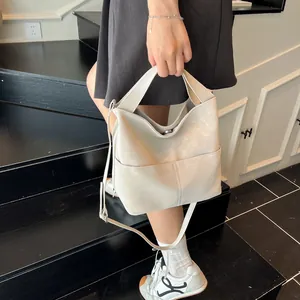 Dettaglio di una borsa tote beige opaca con tasca frontale e sottile tracolla alla moda