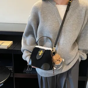 Détail du sac seau en daim noir avec bordure en fausse fourrure blanche et breloque ours