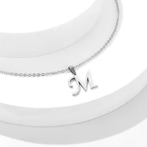 Dettaglio del ciondolo con lettera M d'argento e catena sottile su sfondo minimalista