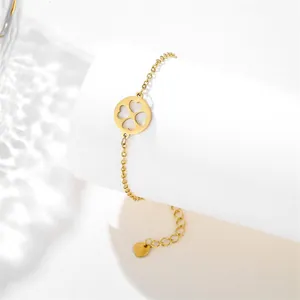 Detail of gold stainless steel bracelet with clover-shaped heart cutout pendant on a stand
