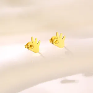 Polished golden OK hand gesture stud earrings in stainless steel on a beige stand