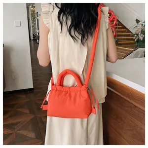 Detail of bright orange puffer crossbody bag showing quilted texture and drawstring accents