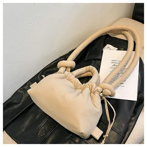 Detailed close-up of beige puffy cloud bag with drawstring and knot strap on black leather
