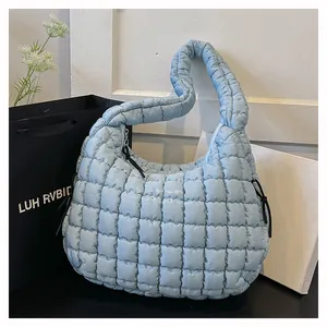 Detail of light blue quilted puffer shoulder bag with square stitching and wide strap