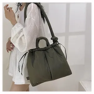 Detail of dark green puffer shoulder bag featuring padded handles and drawstring side